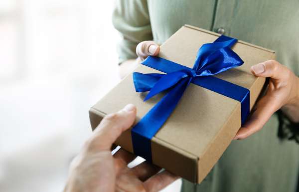 Hand überreicht Geschenk mit blauer Schleife an Person mit grünem Hemd